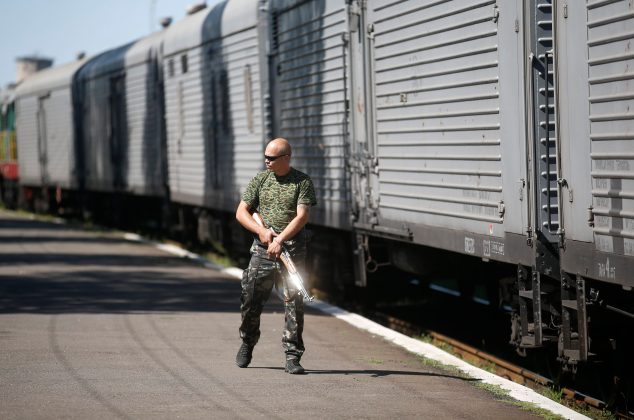 An armed pro-Russian separatist walks near a carriage as monitors from OSCE and members of a forensic team arrive to inspect a train at a railway station in Torez