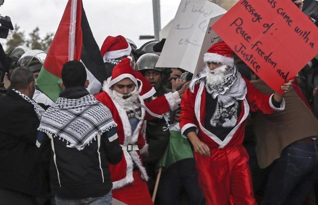 Un grupo de manifestantes disfrazados de Papá Noel protesta durante un enfrentamietnto en un punto de control de Belén (Palestina), hoy, martes 23 de diciembre de 2014. El objetivo de la protesta era pedir el libre acceso a Jerusalén durate las fiestas de Navidad. EFE/Atef Safadi