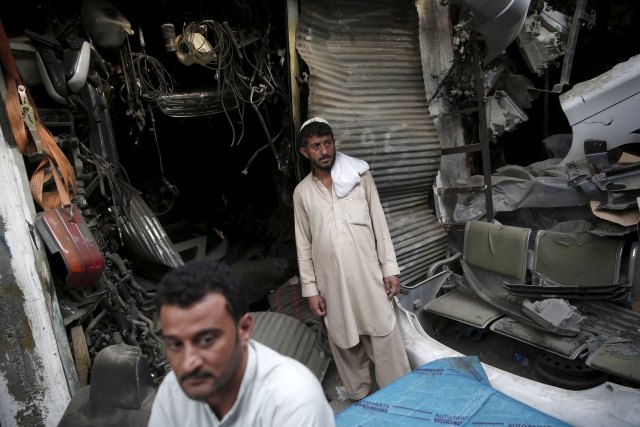 Afghan men stand next to damaged shops near the site of a truck bomb blast in Kabul, Afghanistan