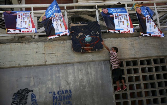 A boy plays basketball next to posters of Venezuela's late President Hugo Chavez in Caracas December 4, 2015. Polarized Venezuela heads to the polls this weekend with a punishing recession forecast to rock the ruling Socialists and propel an optimistic opposition to its first legislative majority in 16 years. REUTERS/Nacho Doce