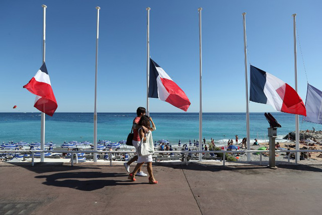 People pass French flags lowered at half-mast in Nice on July 16, 2016, following the deadly Bastille Day attack. The Islamic State group claimed responsibility for the truck attack that killed 84 people in Nice on France's national holiday, a news service affiliated with the jihadists said on July 16. Tunisian Mohamed Lahouaiej-Bouhlel, 31, smashed a 19-tonne truck into a packed crowd of people in the Riviera city celebrating Bastille Day -- France's national day. / AFP PHOTO / Valery HACHE