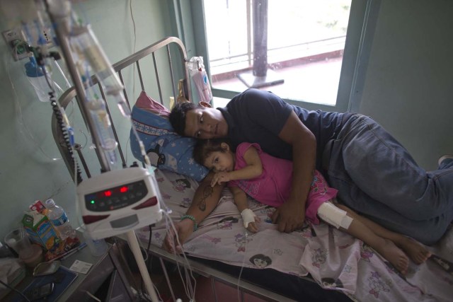En esta imagen del 11 de agosto de 2016, Maykol Pacheco se acurruca con su hija Ashley en su cama de hospital, durante su estancia de dos meses en el Hospital Universitario de Caracas, en Venezuela. (AP Foto/Ariana Cubillos)