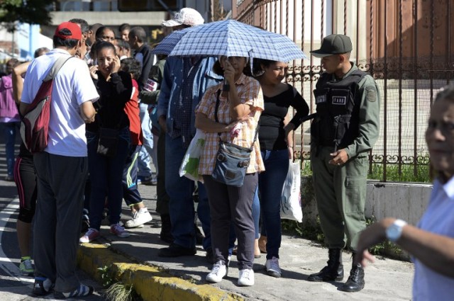 Venezuelan soldiers patrol whilst people queue outside Venezuela's Central Bank (BCV) in Caracas in an attempt to change 100 Bolivar notes, on December 16, 2016. Venezuelans lined up to deposit 100-unit banknotes before they turned worthless, but replacement bills had yet to arrive, increasing the cash chaos in the country with the world's highest inflation. Venezuelans are stuck in currency limbo after President Nicolas Maduro ordered the 100-bolivar note -- the largest denomination, currently worth about three US cents -- removed from circulation in 72 hours. / AFP PHOTO / FEDERICO PARRA