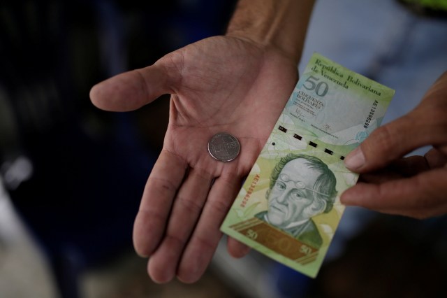 Un comerciante sostiene una moneda de 50 bolívares y un billete de 50 bolívares para esta fotografía tomada en un puesto callejero en el centro de Caracas, Venezuela