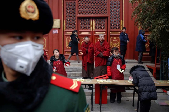 Buddhist monks stand behind a paramilitary policeman providing security as people gather to burn incense sticks and pray for good fortune at Yonghegong Lama Temple on the first day of the Lunar New Year of the Rooster in Beijing, China January 28, 2017. REUTERS/Damir Sagolj