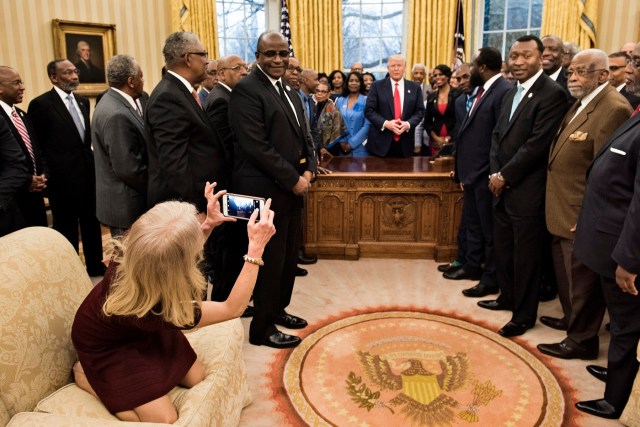 Counselor to the President Kellyanne Conway takes a photo as US President Donald Trump and leaders of historically black universities and colleges talk before a group photo in the Oval Office of the White House before a meeting with US Vice President Mike Pence February 27, 2017 in Washington, DC. / AFP PHOTO / Brendan Smialowski