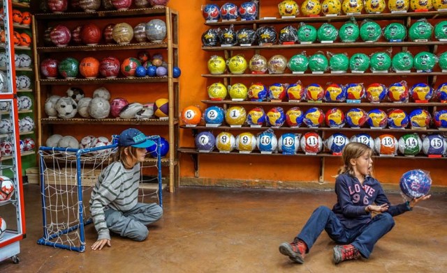 Young tourists play at a ball factory in Mongui, in the Colombian department of Boyaca, on February 13, 2017. Mongui, in the central mountains of Colombia, has about 20 football factories that make balls mainly for football and micro-football. About a quarter of the town's 4,900 inhabitants work in these factories. / AFP PHOTO / Luis ACOSTA