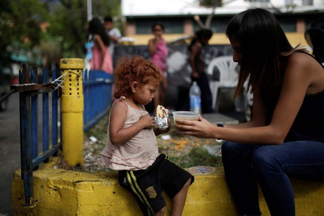 A volunteer of Make The Difference (Haz La Diferencia) charity initiative gives a cup of soup and an arepa to a homeless child  in a street of Caracas, Venezuela March 5, 2017. Picture taken March 5, 2017. REUTERS/Marco Bello