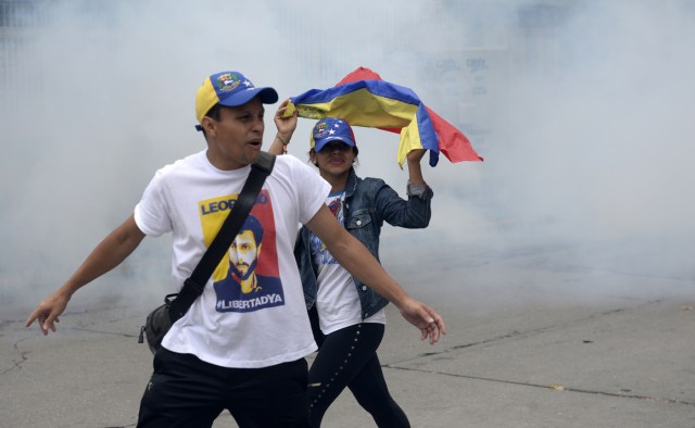 Venezuelan opposition activists run from tear gas shot by police during a march against President Nicolas Maduro, in Caracas on May 1, 2017. May Day protests risk being rough in Venezuela as it marks one month since deadly clashes erupted in a political crisis with no end in sight. Protesters took to the streets from April 1 to demand elections after the courts tried to strengthen President Nicolas Maduro's grip on power. / AFP PHOTO / FEDERICO PARRA