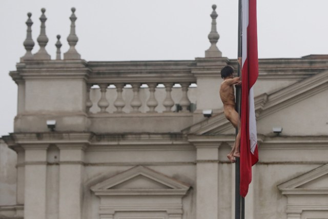 -FOTODELDIA- CHI02. SANTIAGO (CHILE), 25/05/2017.- Un hombre desnudo trepa el mástil de la bandera chilena en frente del Palacio de La Moneda hoy, jueves 25 de mayo de 2017, en Santiago (Chile). En una inusual protesta, de la que se desconocen hasta el momento los motivos, el hombre permaneció varios minutos en el mástil hasta que se lanzó y cayó sobre un autobús de los carabineros de la policía chilena, quienes aseguraron que el sujeto tiene problemas mentales. EFE/Marcelo Rodríguez