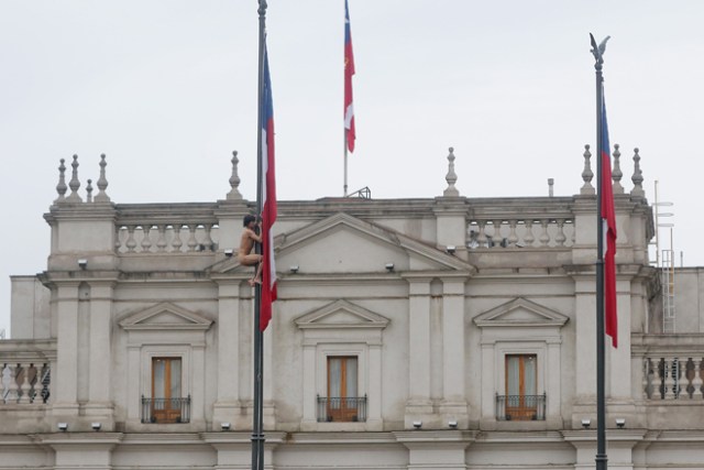 CHI01. SANTIAGO (CHILE), 25/05/2017.- Un hombre desnudo trepa el mástil de la bandera chilena en frente del Palacio de La Moneda hoy, jueves 25 de mayo de 2017, en Santiago (Chile). En una inusual protesta, de la que se desconocen hasta el momento los motivos, el hombre permaneció varios minutos en el mástil hasta que se lanzó y cayó sobre un autobús de los carabineros de la policía chilena, quienes aseguraron que el sujeto tiene problemas mentales. EFE/Marcelo Rodríguez