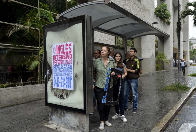 Laura Castillo (L), Abril Mejias (C) and Dereck Blanco wait for a bus to give an on-board presentation of the Bus TV news in Caracas, Venezuela, on June 6, 2017. A group of young Venezuelan reporters board buses to present the news, as part of a project to keep people informed in the face of what the opposition and the national journalists' union describe as censorship by the government of Nicolas Maduro. / AFP PHOTO / LUIS ROBAYO