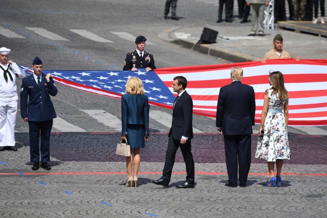 (RtoL) US First Lady Melania Trump, US President Donald Trump, French President Emmanuel Macron and his wife Brigitte Macron, stand in front of the US national flag held by soldiers, at the end of the annual Bastille Day military parade on the Champs-Elysees avenue in Paris on July 14, 2017. The parade on Paris's Champs-Elysees will commemorate the centenary of the US entering WWI and will feature horses, helicopters, planes and troops. / AFP PHOTO / ALAIN JOCARD