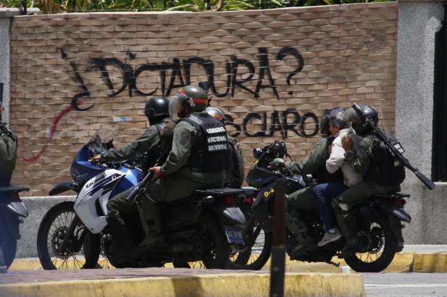 Soldiers on motorcycles carry a person past a sign that says "Dictatorship?" as the Constituent Assembly election was being carried out in Caracas, Venezuela, July 30, 2017. REUTERS/Carlos Garcia Rawlins