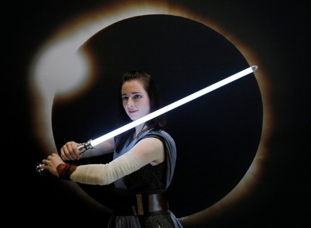 A woman dressed as Rey from the upcoming Star Wars movie "The Last Jedi" poses for a photograph in front of an image of a solar eclipse at the Eclipse Comic-Con at Southern Illinois University in Carbondale, Illinois, U.S., August 20, 2017 one day before a total solar eclipse in the city. REUTERS/Brian Snyder