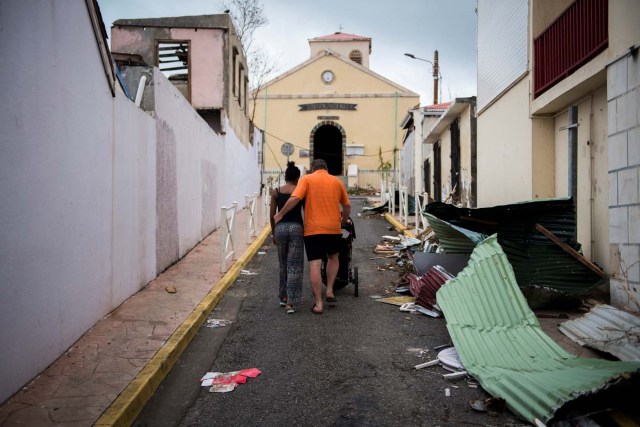 A couple walks in the streets of Marigot, on September 9, 2017 in Saint-Martin island devastated by Irma hurricane. Officials on the island of Guadeloupe, where French aid efforts are being coordinated, suspended boat crossings to the hardest-hit territories of St. Martin and St. Barts where 11 people have died. Two days after Hurricane Irma swept over the eastern Caribbean, killing at least 17 people and devastating thousands of homes, some islands braced for a second battering from Hurricane Jose this weekend. / AFP PHOTO / Martin BUREAU