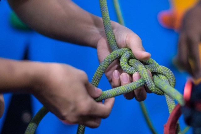 In this photograph taken on August 16, 2017, Khin Myat Thu Zar, a 32-year-old former lawyer who has been teaching yoga in Myanmar professionally for the last five years, loops climbing rope into a knot while attaching a harness to a student before the student performs yoga poses during class at a studio in Yangon. First there was beer and paddleboard yoga. Then someone added goats to the mix. Now fitness buffs in Myanmar are taking the latest body-bending trend to whole new heights -- pulling off yoga poses on a climbing wall. / AFP PHOTO / Roberto SCHMIDT / TO GO WITH AFP STORY MYANMAR-LIFESTYLE-SPORT-YOGA-CLIMBING,FEATURE BY ATHENS ZAW ZAW