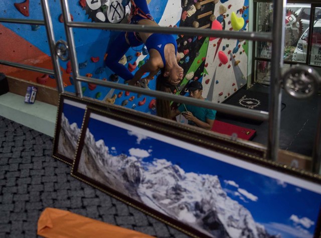 In this photograph taken on August 16, 2017, Khin Myat Thu Zar (C), a 32-year-old former lawyer who has been teaching yoga in Myanmar professionally for the last five years, performs a yoga pose on a climbing wall during a class at a studio in Yangon. First there was beer and paddleboard yoga. Then someone added goats to the mix. Now fitness buffs in Myanmar are taking the latest body-bending trend to whole new heights -- pulling off yoga poses on a climbing wall. / AFP PHOTO / Roberto SCHMIDT / TO GO WITH AFP STORY MYANMAR-LIFESTYLE-SPORT-YOGA-CLIMBING,FEATURE BY ATHENS ZAW ZAW