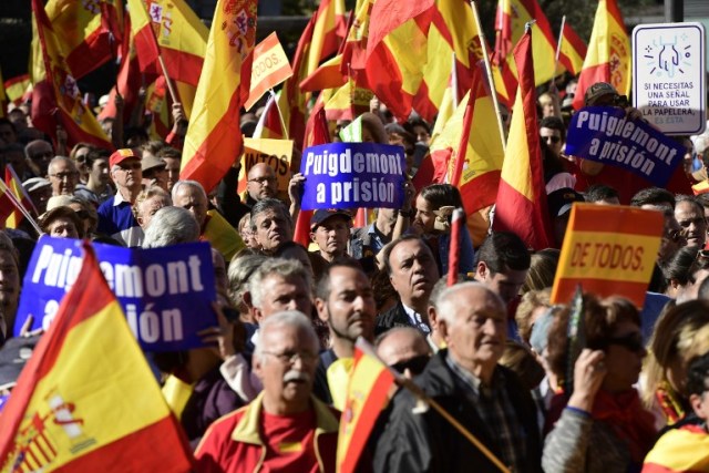 La gente sostiene carteles que leen "(presidente regional catalán Carles) Puigdemont a prisión" mientras agitaba banderas españolas durante una manifestación llamando a la unidad en la Plaza de Colón en Madrid el 28 de octubre de 2017, un día después de que se impuso el control directo sobre Cataluña por un intento de separarse de España. España se movió para afirmar el dominio directo sobre Cataluña, reemplazando a sus funcionarios ejecutivos y altos para sofocar un impulso de independencia que ha sumido al país en una crisis y ha puesto nerviosa a la Europa secesionista. / AFP PHOTO / JAVIER SORIANO