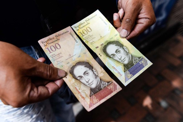 A man holds the new one hundred thousand-Bolivar-note (R) comparing it to the one hundred note, to show the resemblance between both bills in Caracas on November 9, 2017. The new bill is worth 29,89 US dollars in the official market and 2 dollars in the black market at November 9, 2017 exchange rate. / AFP PHOTO / FEDERICO PARRA