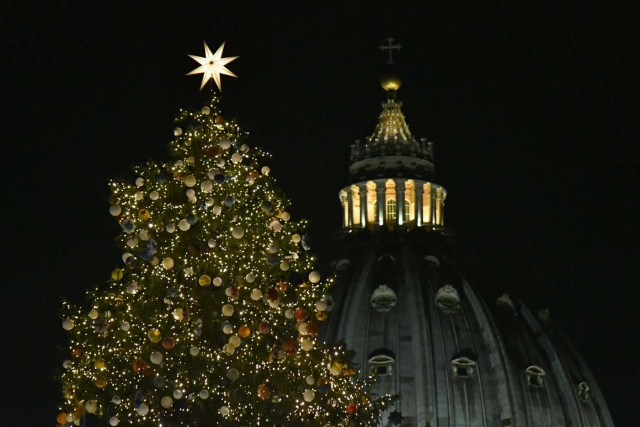 The christmas tree of St Peter's square is illuminated with the dome of St Peter's basilica in the background during the inauguration of the christmas crib on December 7, 2017 in Vatican. / AFP PHOTO / Alberto PIZZOLI