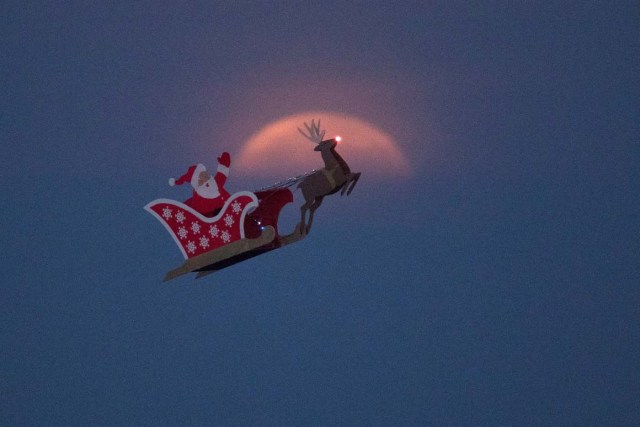 A 10-foot long remote controlled flying Santa makes a test flight past a setting moon over the ocean in Carlsbad, California, U.S., December 3, 2017.      REUTERS/Mike Blake