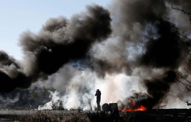 A Palestinian protester is seen as smoke rises from burning tires during clashes with Israeli troops as Palestinians call for a "day of rage" in response to U.S. President Donald Trump's recognition of Jerusalem as Israel's capital, near the Jewish settlement of Beit El, near the West Bank city of Ramallah December 8, 2017. REUTERS/Mohamad Torokman