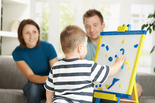 Father, mother and boy child playing together with toy whiteboard, learning letters and numbers.
