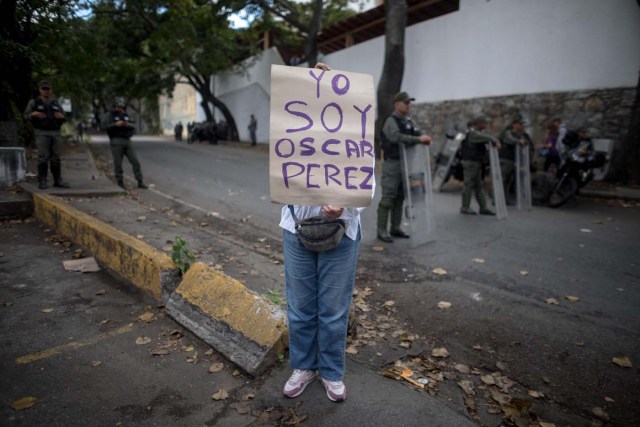 CAR12. CARACAS (VENEZUELA), 17/01/2018.- Una mujer sostiene un cartel en el que se lee "Yo soy Óscar Pérez" junto a miembros de la Guardia Nacional Bolivariana y la Policía Nacional Bolivariana que custodian las inmediaciones de la morgue en donde está cuerpo del exagente Pérez hoy, miércoles 17 de enero de 2018, en Caracas (Venezuela). Decenas de agentes de la Policía Nacional Bolivariana custodian desde la mañana de hoy los alrededores de la principal morgue de Caracas, después de que familiares de Óscar Pérez, el exagente alzado contra el Gobierno chavista quien falleció el lunes, exigieran identificar su cuerpo. EFE/MIGUEL GUTIÉRREZ