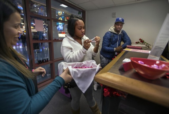 Employee Bianca Dozal offers a bracelet gift to Teaira Thompson and James Anderson of Burlington, Iowa, who completed their paperwork as the Clark County Clerk's Office operates a temporary pop-up marriage license office at McCarran International Airport in Las Vegas on February 12, 2018. The Las Vegas airport has given new meaning to rushing to make a connection, offering quickie wedding licenses for lovebirds desperate to get hitched on Valentine's Day. Clark County, the authority that administers Sin City's weddings, has opened a pop-up marriage license bureau by a baggage carousel at McCarran International Airport. / AFP PHOTO / L.E. Baskow / TO GO WITH AFP STORY, "Valentines get quickie marriage licenses at Las Vegas airport"