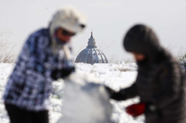People play with the snow as Saint Peter's Basilica dome is seen in the background after a heavy snowfall in Rome, Italy February 26, 2018. REUTERS/Alessandro Bianchi