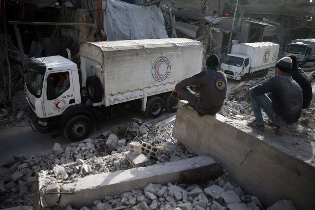 Los miembros de la defensa civil se sientan entre los escombros mientras miran un convoy de ayuda de la Media Luna Roja Árabe Siria conduciendo a través de la ciudad sitiada de Douma, Ghouta Oriental, Damasco, Siria el 5 de marzo de 2018. REUTERS / Bassam Khabieh