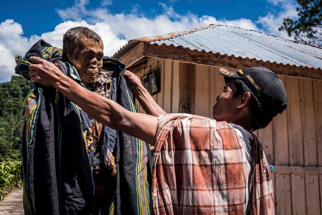 PIC BY Claudio Sieber / CATERS NEWS - (PICTURED A relative is dressing up his ancestor during the ritual of MaNene)THESE images show a unique insight into the village where the living dig up their dead relatives to clean their bones and to dress them up. The dead can even remain in homes for decades until the family throw a huge party in their honour. The corpses are treated as sick until they finally find peace after funeral rites known as Rambu Solo The bizarre ritual was pictured in South Sulawesi, Indonesia, where even buried relatives are taken out of their coffins for new outfits and a bone polish. SEE CATERS COPY