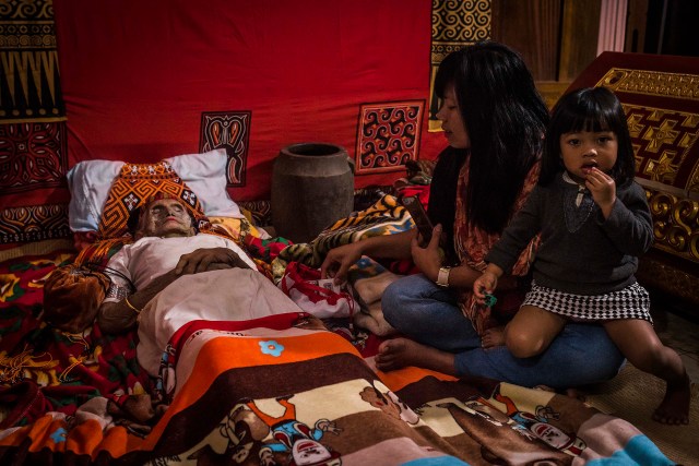 PIC BY Claudio Sieber / CATERS NEWS - (PICTURED Relatives visit Nene Tiku who passed away 3 days ago in the age of 106. Her relatives believe, Nene Tiku is only sick - not dead )THESE images show a unique insight into the village where the living dig up their dead relatives to clean their bones and to dress them up. The dead can even remain in homes for decades until the family throw a huge party in their honour. The corpses are treated as sick until they finally find peace after funeral rites known as Rambu Solo The bizarre ritual was pictured in South Sulawesi, Indonesia, where even buried relatives are taken out of their coffins for new outfits and a bone polish. SEE CATERS COPY