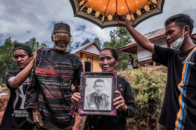 PIC BY Claudio Sieber / CATERS NEWS - (PICTURED Family is presenting Djim Sambara, who died 2 years ago when 90. He was honorably buried in his military uniform. As it is usual for Torajans to honor the death to bury them in the clothes they most liked.)THESE images show a unique insight into the village where the living dig up their dead relatives to clean their bones and to dress them up. The dead can even remain in homes for decades until the family throw a huge party in their honour. The corpses are treated as sick until they finally find peace after funeral rites known as Rambu Solo The bizarre ritual was pictured in South Sulawesi, Indonesia, where even buried relatives are taken out of their coffins for new outfits and a bone polish. SEE CATERS COPY