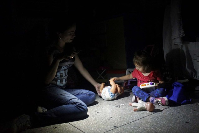 Monica Lizcano uses light from a phone while she plays with her daughter Valentina, during a blackout in San Cristobal, Venezuela, April 19, 2018. Picture taken April 19, 2018. REUTERS/Carlos Eduardo Ramirez