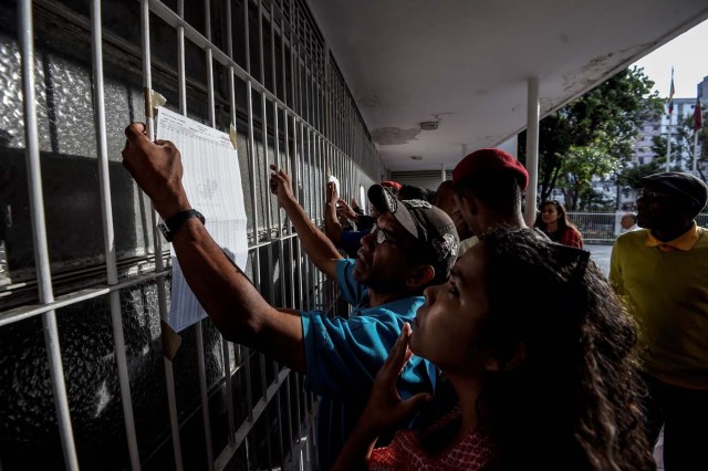 Venezuelans look for their names moments before casting their vote at a polling station during presidential elections in Caracas on May 20, 2018 Venezuelans, reeling under a devastating economic crisis, began voting Sunday in an election boycotted by the opposition and condemned by much of the international community but expected to hand deeply unpopular President Nicolas Maduro a new mandate / AFP PHOTO / Juan BARRETO