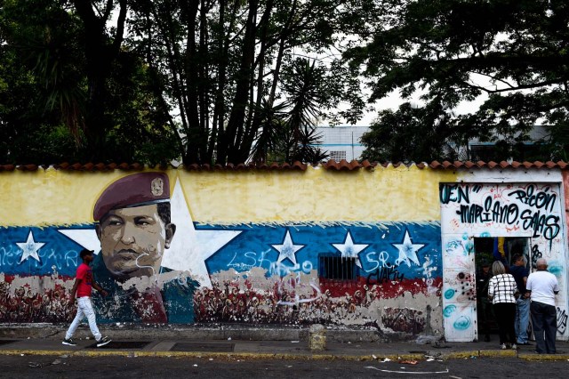A man walks in front of an image of late Venezuelan president Hugo Chavez as peole wait to enter a polling station to cast their vote during the presidential elections in Caracas on May 20, 2018 Venezuelans, reeling under a devastating economic crisis, began voting Sunday in an election boycotted by the opposition and condemned by much of the international community but expected to hand deeply unpopular President Nicolas Maduro a new mandate / AFP PHOTO / FEDERICO PARRA