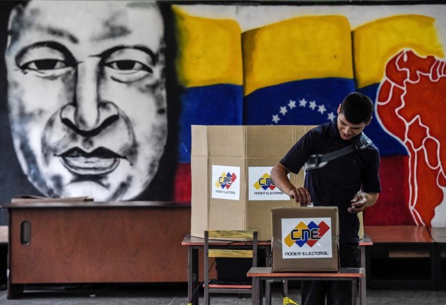 A man casts his vote in front of an image of late Venezuelan president Hugo Chavez, during the presidential elections at a polling station in Caracas on May 20, 2018 Venezuelans, reeling under a devastating economic crisis, began voting Sunday in an election boycotted by the opposition and condemned by much of the international community but expected to hand deeply unpopular President Nicolas Maduro a new mandate / AFP PHOTO / Juan BARRETO