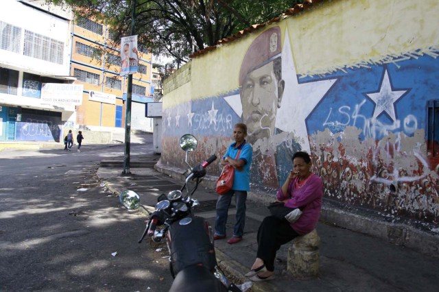 Women wait by a mural of the late Venezuelan President Hugo Chavez during the presidential election in Caracas, Venezuela, May 20, 2018. REUTERS/Adriana Loureiro Fernandez